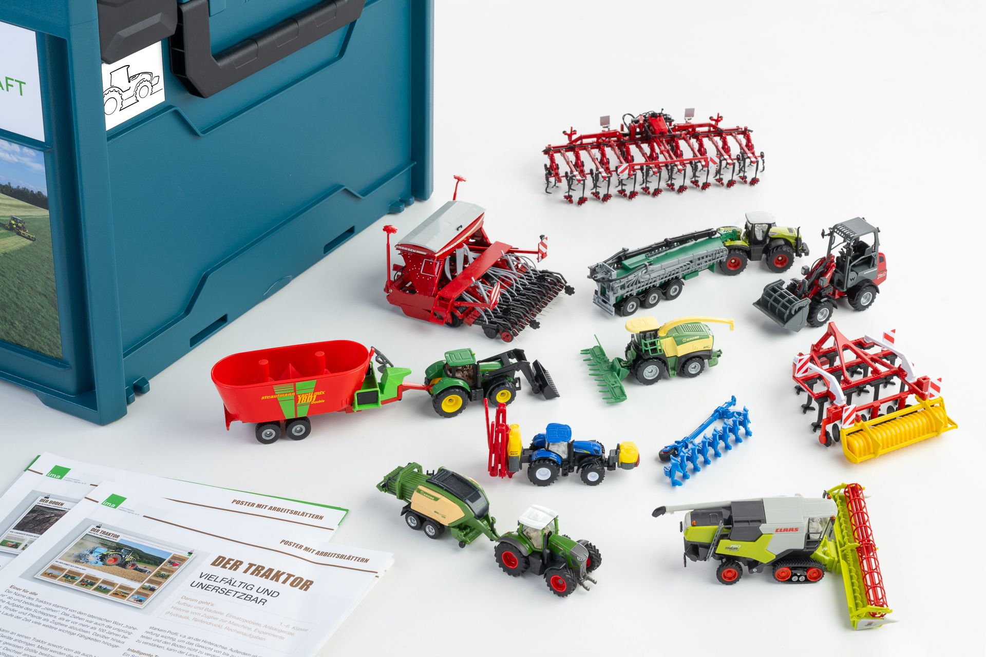 Miniaturmodelle landwirtschaftlicher Geräte und Fahrzeuge vor einem Koffer.