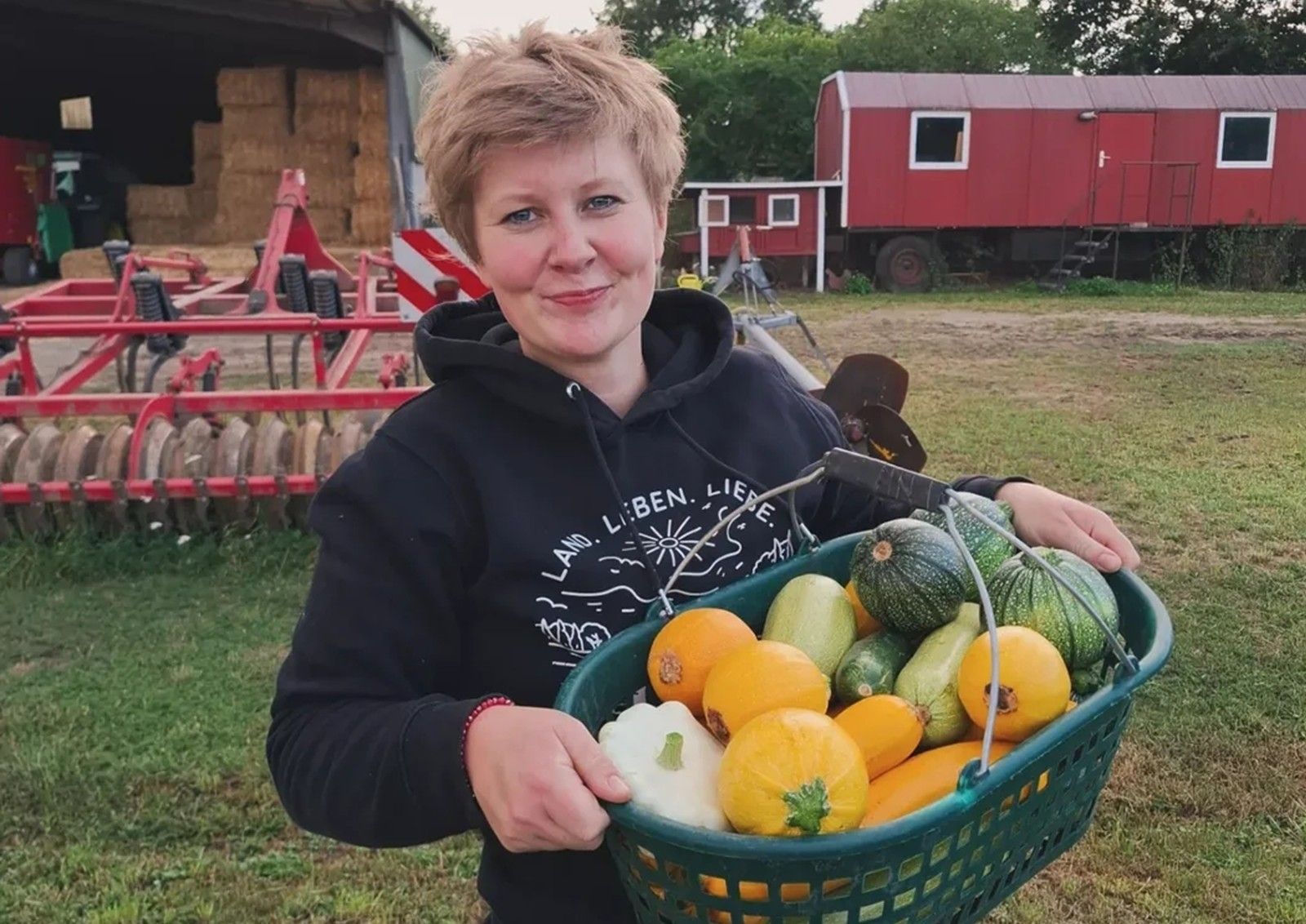 Charlotte Schlichting trägt einen Korb mit Feldfrüchten.